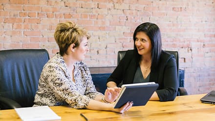 Two professionals in HR roles at an office table, reviewing information on a tablet.