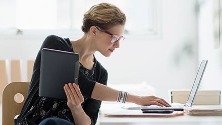 A woman researching whether an MBA is worth it on her laptop while holding a tablet