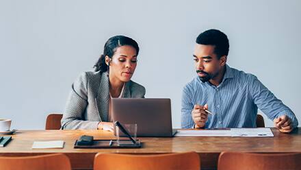 Two people wearing professional clothes looking at a laptop to see if an online associate in finance is worth it