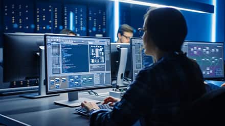 A woman with a ponytail and glasses coding in a computer lab.