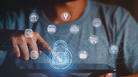 A person using a tablet with icons hovering in the air, including a blue lock to represent cybersecurity.