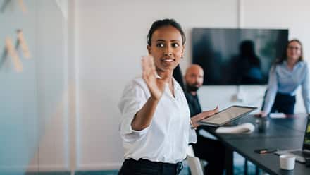 A professional at a white board, presenting the different jobs for master's in communication graduates to a man and a woman in a conference room.