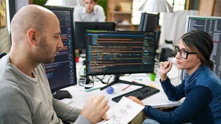 A computer science professional discussing a workflow diagram with a colleague who has code on her desktop.