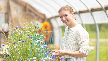 Kayla Stoll, an environmental science student at SNHU, with plants in a greenhouse.
