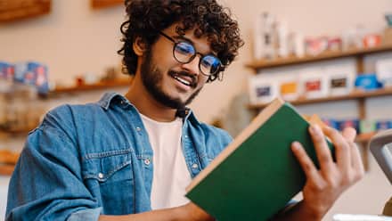 A man reading a book with a green cover.