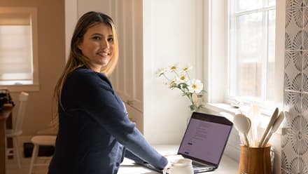 SNHU alum Juliana Zambrano '24, standing at a desk working on her laptop, researching college majors, minors and concentrations.