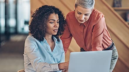 Two management accountants discussing information on one of their a laptops.