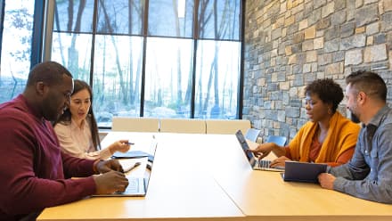 Four business professionals working in pairs at a conference table, discussing MBA vs MS degrees.
