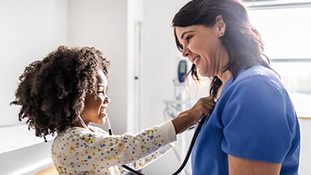A child testing a stethoscope on her nurse, who has the nursing acronym RN