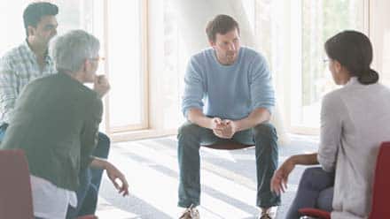 A psychologist and group of clients sitting in a circle during a group therapy session