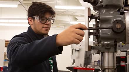 A STEM major wearing goggles and working with machinery.