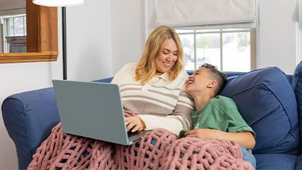 SNHU graduate Madison Richards and her son Malakai sitting on a couch while she works on a laptop, completing her online degree program.