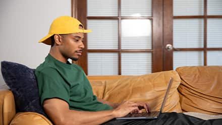 Keyon Tuiteleleapaga, an SNHU graduate with a bachelor's in human services and master's in psychology, using a laptop on his couch.
