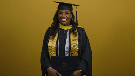 An SNHU graduate wearing an honor society stole and holding her diploma at her commencement ceremony.