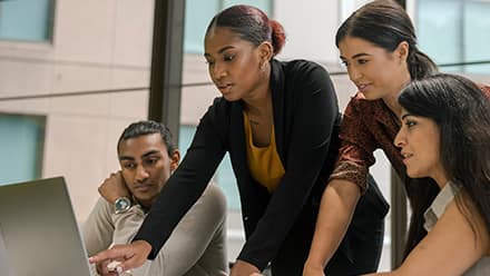 Four professionals with business degrees reviewing information on a laptop.