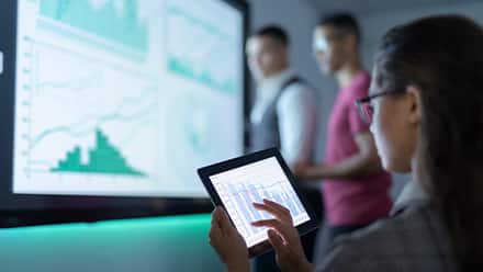 A woman with dark hair and glasses looking at data about what you can do with a finance degree on a tablet.