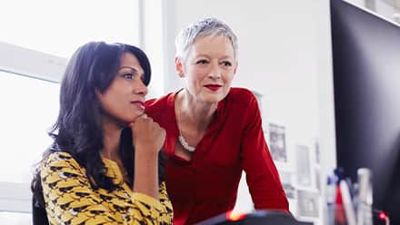 Two women sitting in front of a desktop while considering what you can do with an MBA