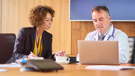 A public health professional discussing a project with a doctor as they both look at a laptop