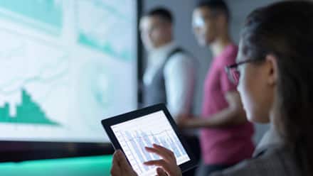 Data analyst looking at a tablet with data charts on it.