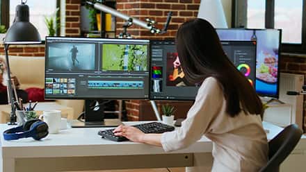 A game developer editing gameplay footage on a multi-monitor workstation.