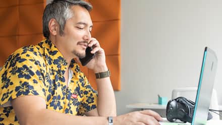 A student working on his Bachelor of Arts degree on his laptop while on a phone call with his advisor