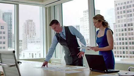 Two master's degree holders discussing documents in a conference room overlooking the city.