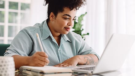  An MA student sitting at a desk taking notes off a laptop