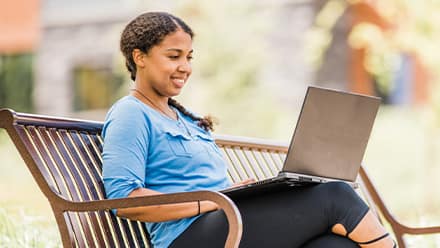A person sitting on a bench, researching what an undergraduate degree is on a laptop.