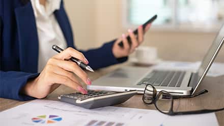 A person sitting at a desk with a laptop and calculator bookkeeping.