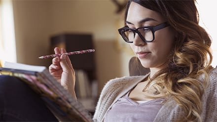 A woman wearing glasses reading a creative writing piece in a notebook.