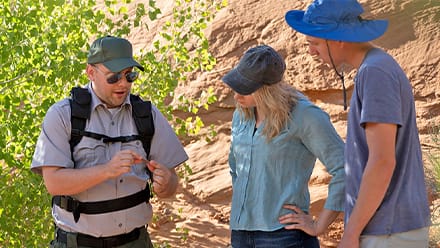SNHU graduate Jon Roos '18, left, working in a park, showing a rock to two park visitors.