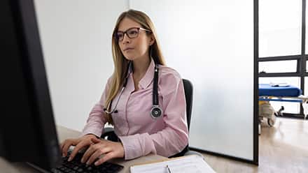 A medical professional wearing a stethoscope and researching what healthcare administration is on her computer.