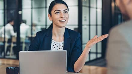 A woman sitting behind a laptop speaking to a man about HR.