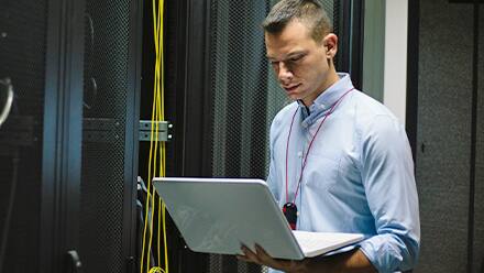 Man working as IT manager standing in a server room working on a laptop 