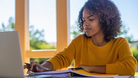 A student in a yellow sweater sitting at a desk working on her minor on her laptop