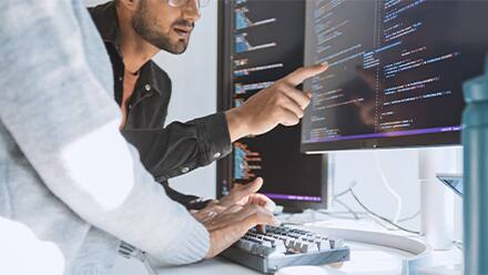 Two computer programmers using Python and reviewing code on a desktop computer.