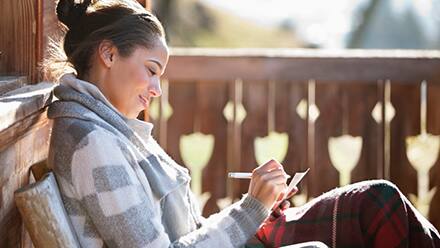 A woman sitting on her deck, practicing self-care by journaling.