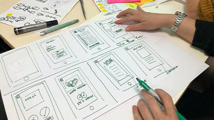 A web designer sketching out different design ideas with a green marker