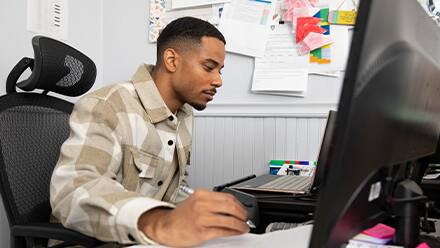  Keyon Tuiteleleapaga, an SNHU master's in psychology alum, sitting at a desk working on his desktop. 