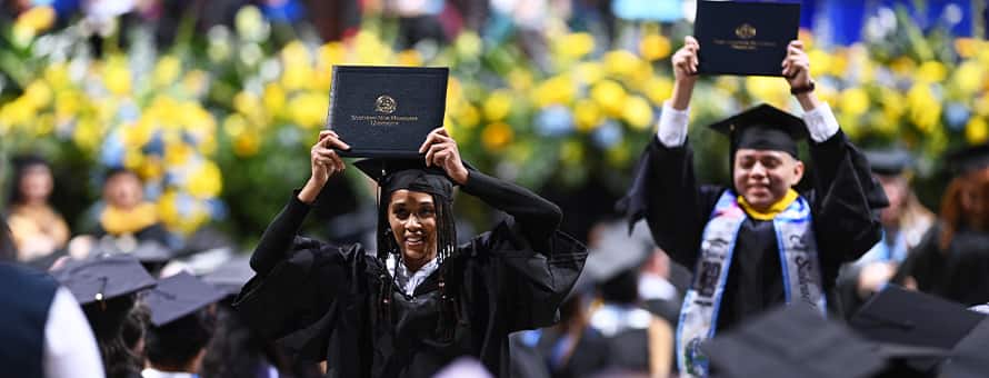 Two SNHU graduates holding up their diplomas at the Fall 2025 commencement ceremony.