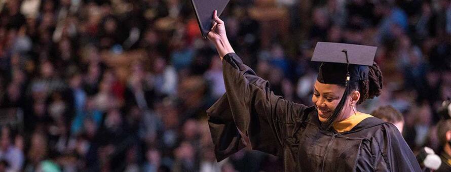 A graduate wearing a cap and gown, holding up her diploma at an SNHU Commencement ceremony