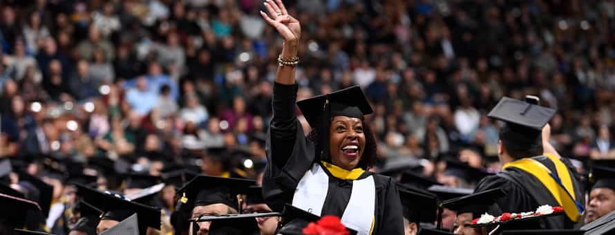 A graduate dressed in cap and gown, waving to loved ones at an SNHU Commencement ceremony.