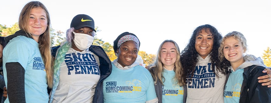 A group of six SNHU students, four wearing SNHU Homecoming shirts and two wearing SNHU Penmen shirts.