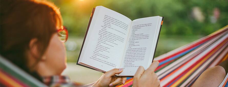 A woman sitting in a hammock during the summer reading her favorite book