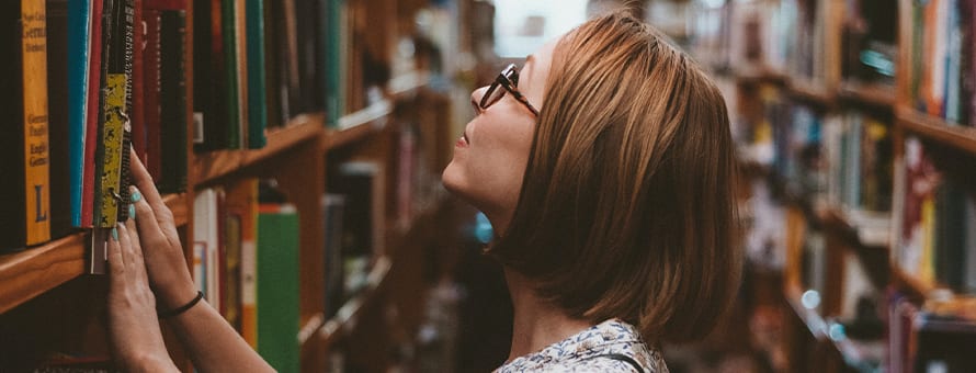 A person browsing books on a tall bookshelf in a library.