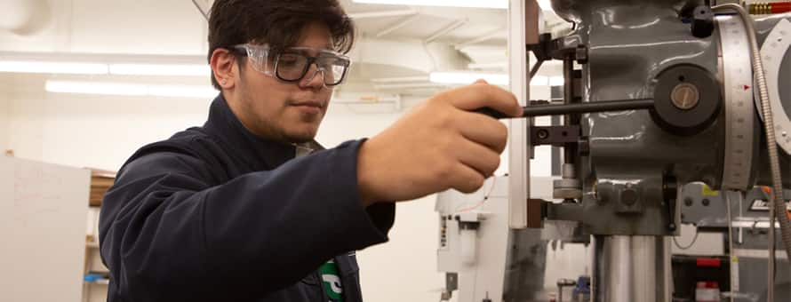 A STEM major wearing goggles and working with machinery. 