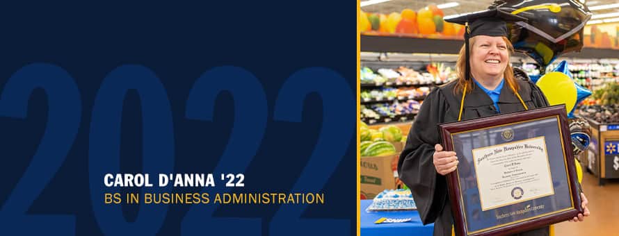Carol D'Anna in her cap and gown holding her diploma, standing in the center of Walmart produce section with a blue banner on the left with the text Carol D'Anna '22 BS in Business Administration with a faded 2022 in the background. 