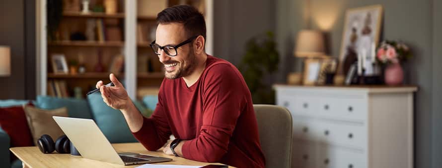 A man sitting at a desk smiling and working on his laptop while earning an English degree.