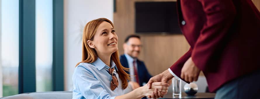 A professionally dressed woman shaking someone's hand in an office setting to represent entry-level HR jobs.