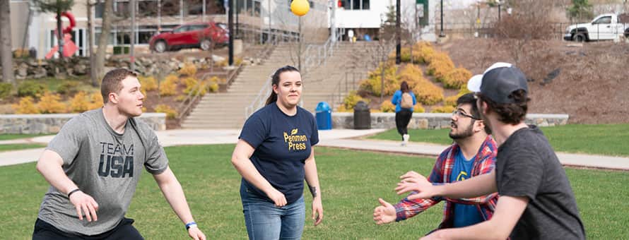A group of college students playing a lawn game on the campus quad.